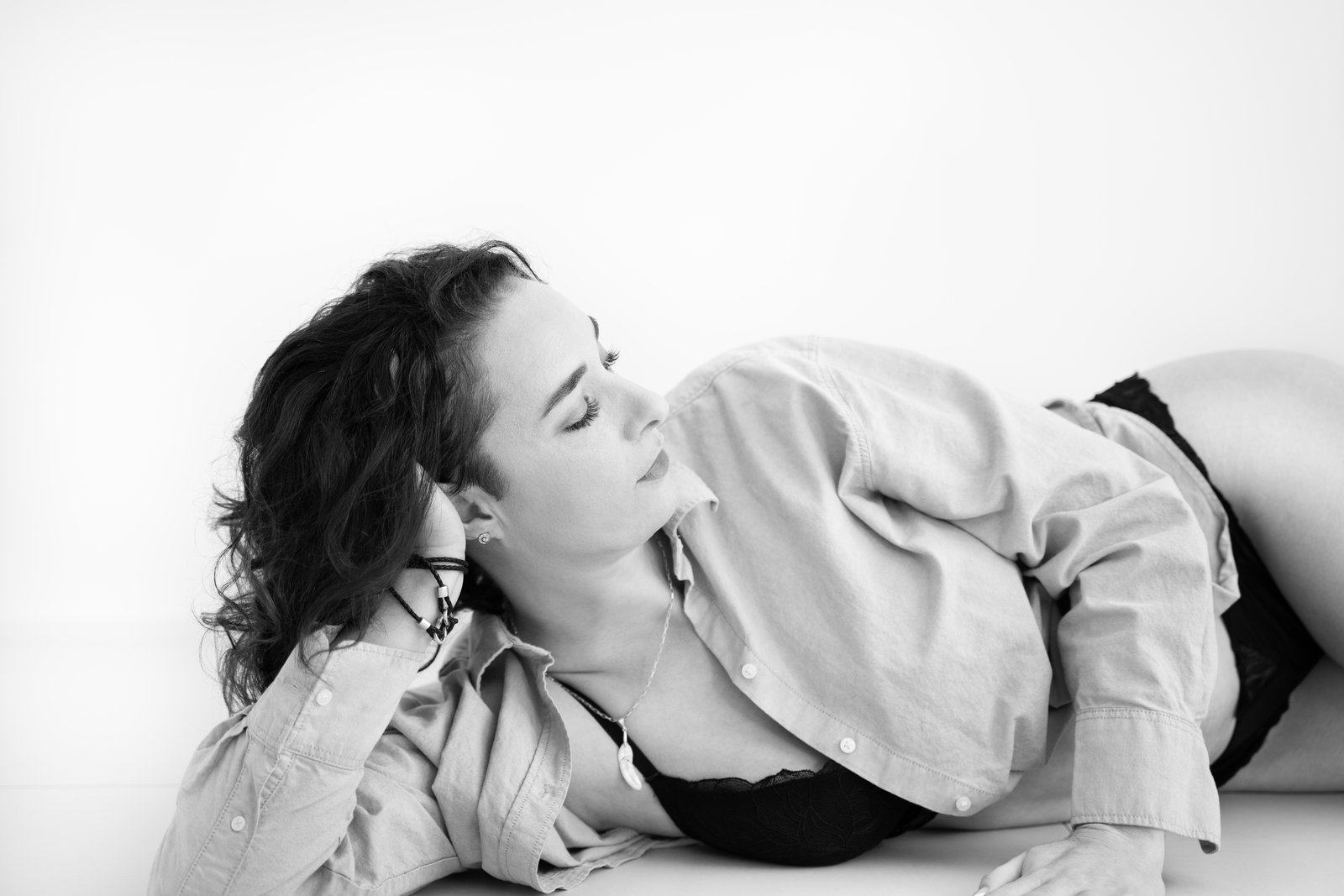 Black and white boudoir photograph of a woman lying in an open shirt