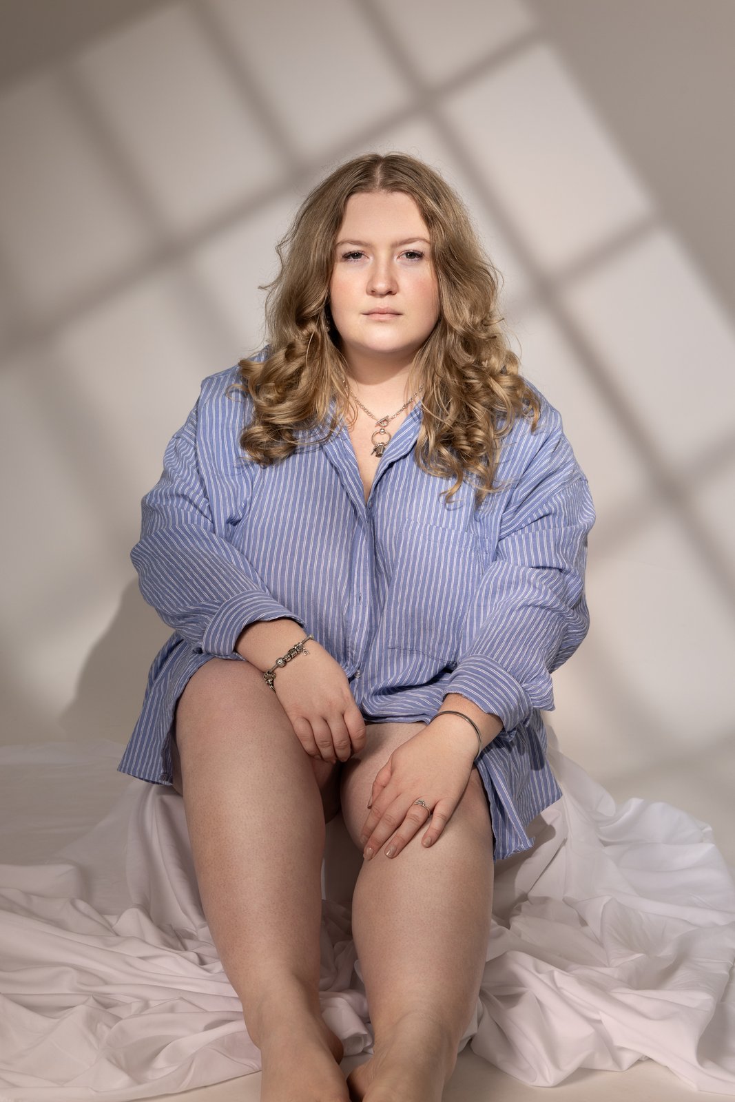 Curvy boudoir portrait in an oversized blue shirt in natural window light