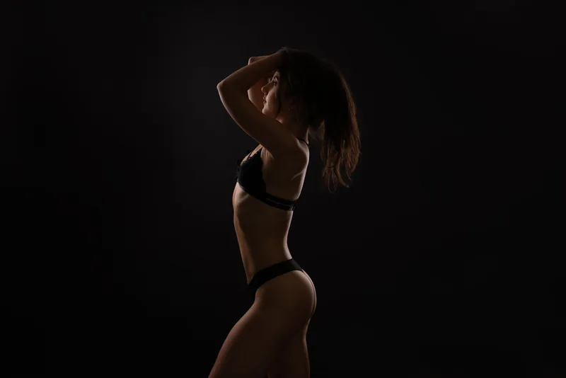 Low key boudoir photograph of a woman standing in profile