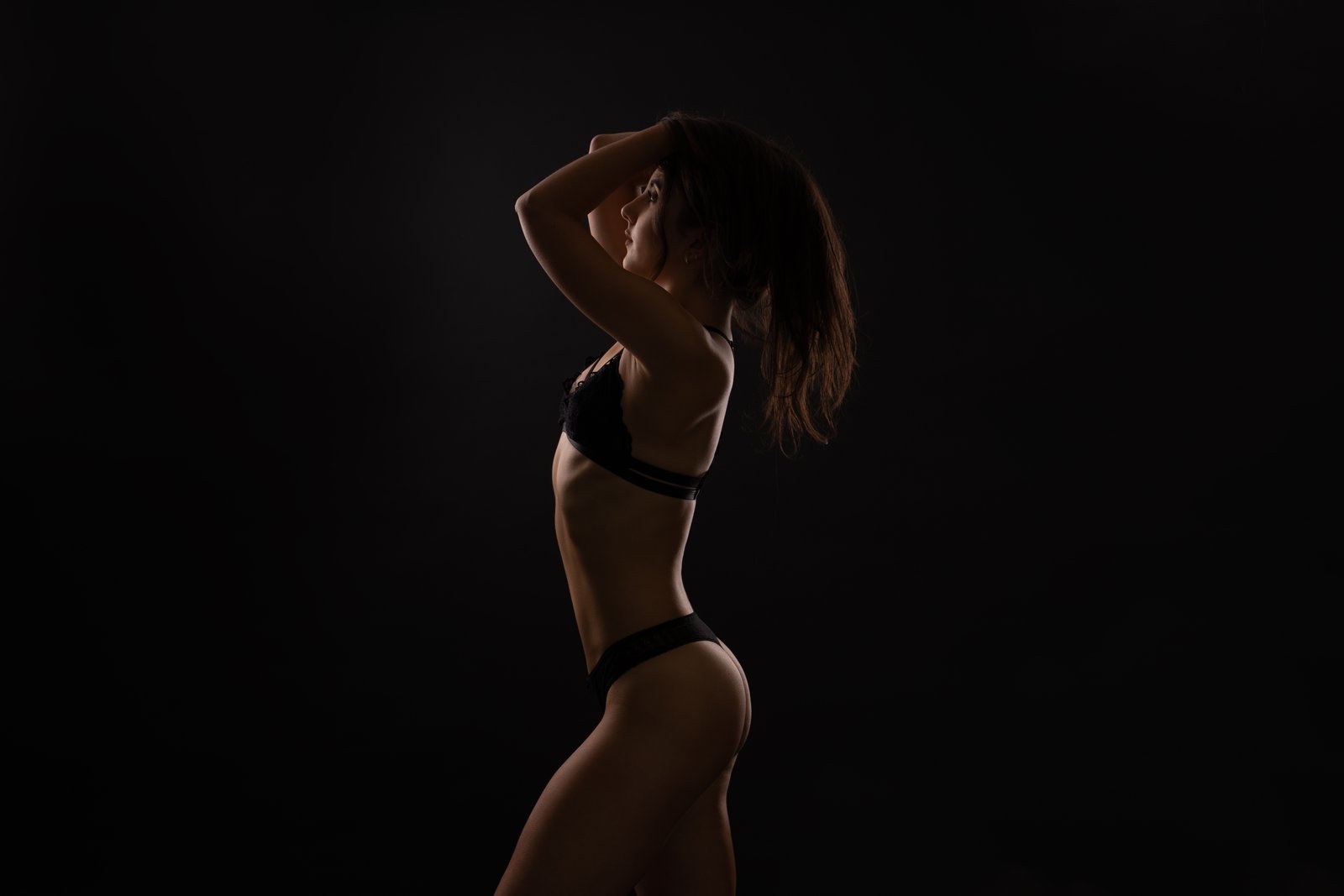 Low key boudoir photograph of a woman standing in profile